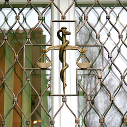 Kované váhy ako symbol lekárstva na okenných mrežiach - detail Kované váhy ako symbol lekárstva na okenných mrežiach - detail